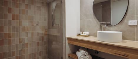 A modern bathroom with a glass-enclosed shower, a round mirror, a sink, and neatly folded towels on a shelf.