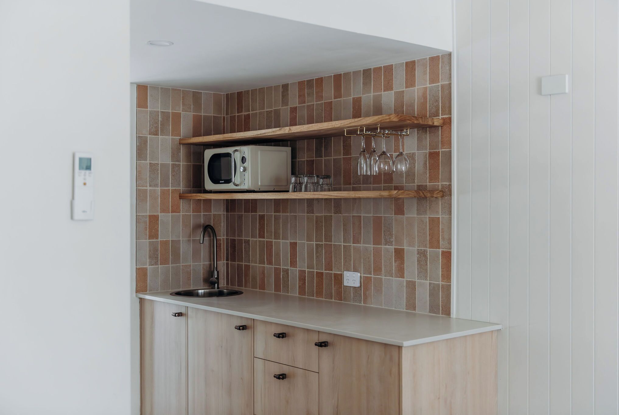 Cocina compacta con microondas, copas de vino y un lavabo.