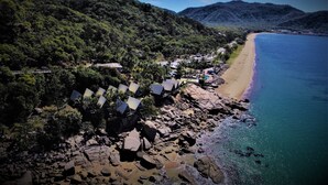 Una zona costera con playa rocosa, una hilera de cabañas de playa y montañas al fondo.