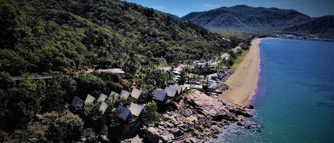 Una zona costera con playa rocosa, una hilera de cabañas de playa y montañas al fondo.