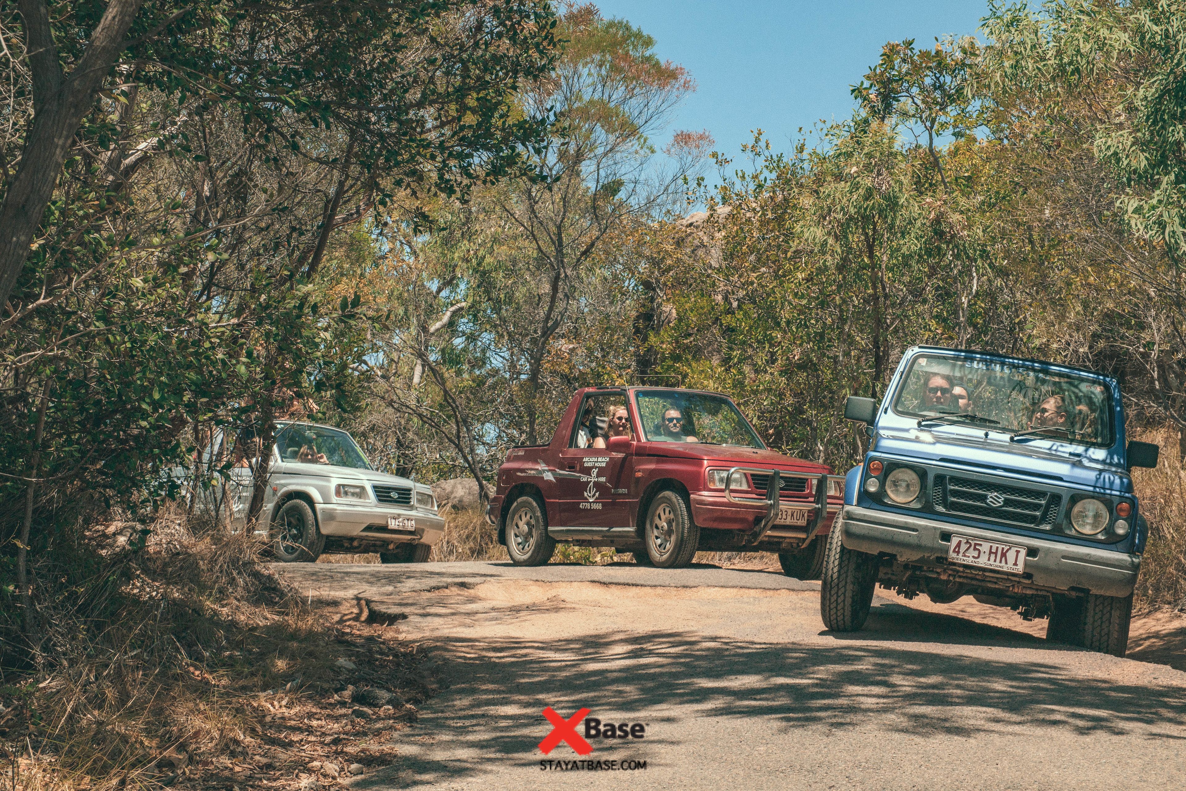 Três veículos numa estrada de terra rodeados por árvores.