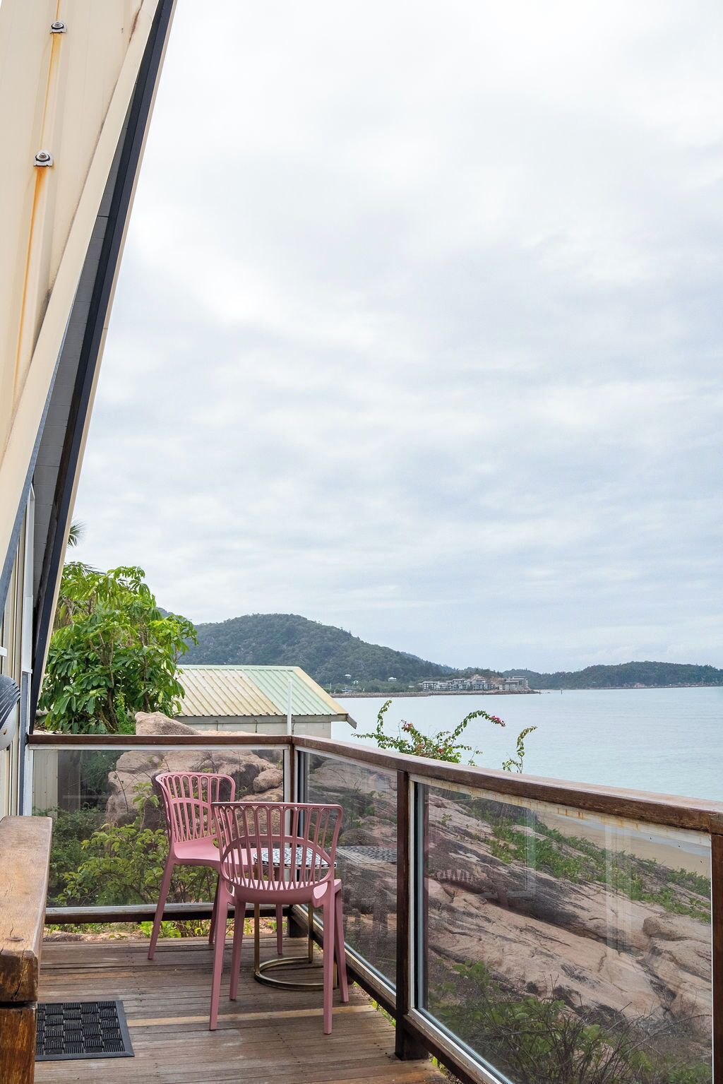 A balcony with two pink chairs, overlooking a body of water and a distant shoreline.