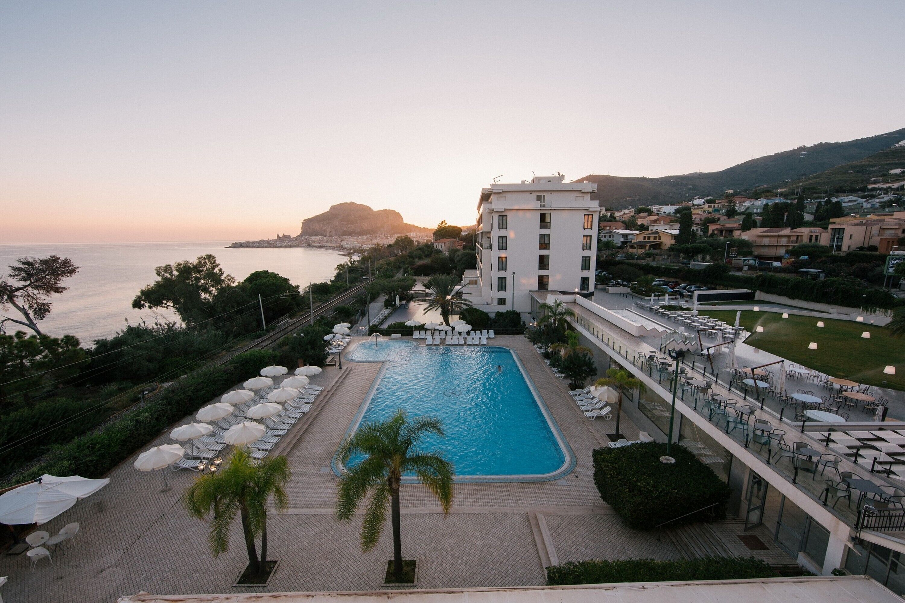 A resort with a swimming pool, outdoor seating, and a view of the sea.