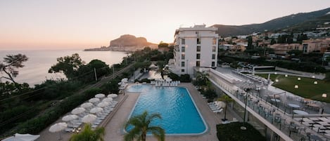 A resort with a swimming pool, outdoor seating, and a view of the sea.