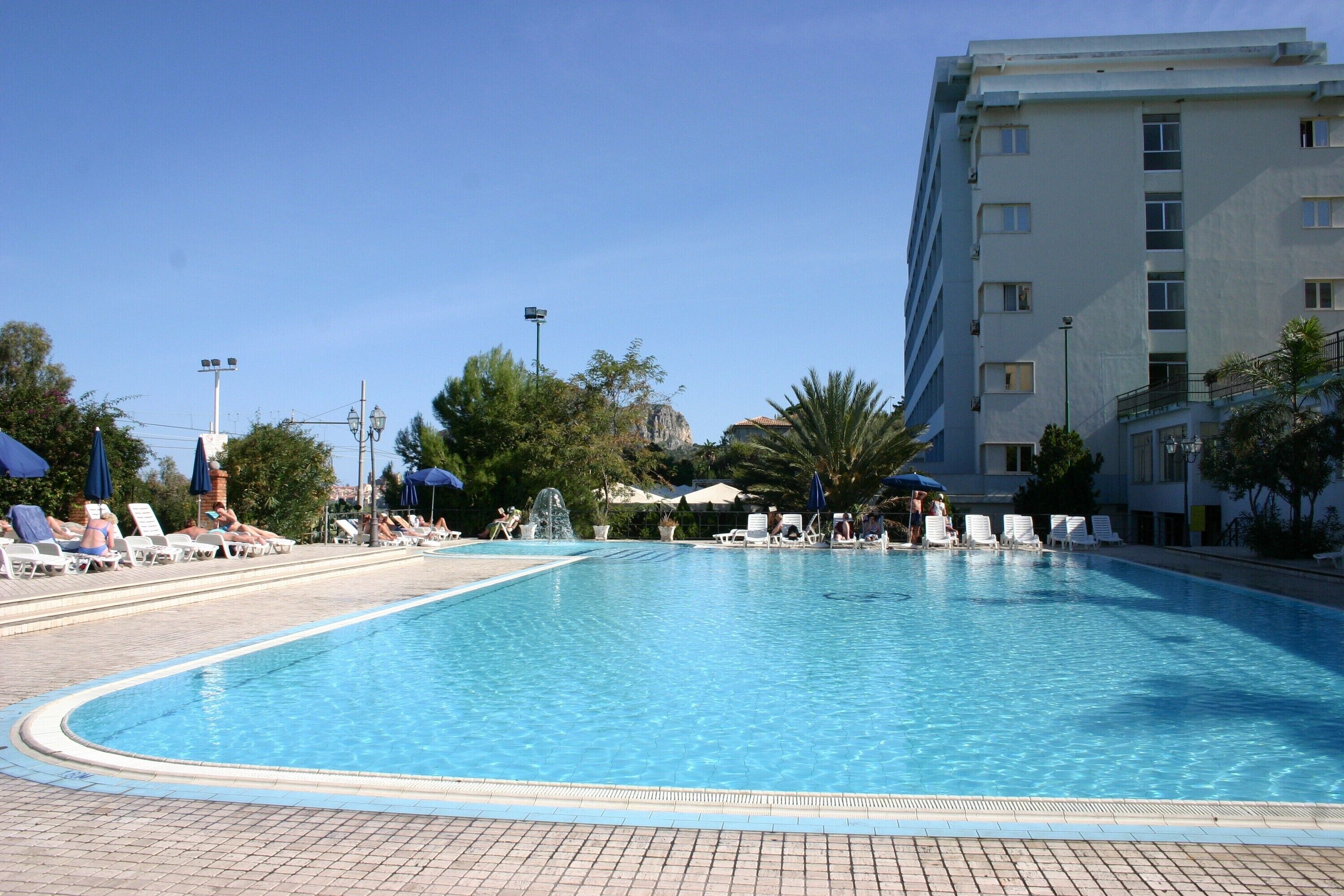 A swimming pool with lounge chairs and umbrellas, surrounded by trees and a building.