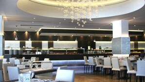 Ein modernes Restaurant mit einer zentralen Bar, weißen Stühlen und einem außergewöhnlichen Kronleuchter.