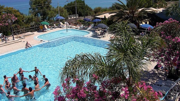 Ein Swimmingpool mit Blick auf das Meer, umgeben von Palmen und Liegestühlen.