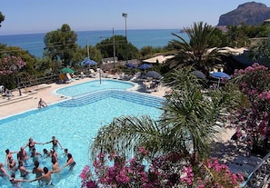 Une piscine avec vue sur la mer, entourée de palmiers et de chaises de plage.