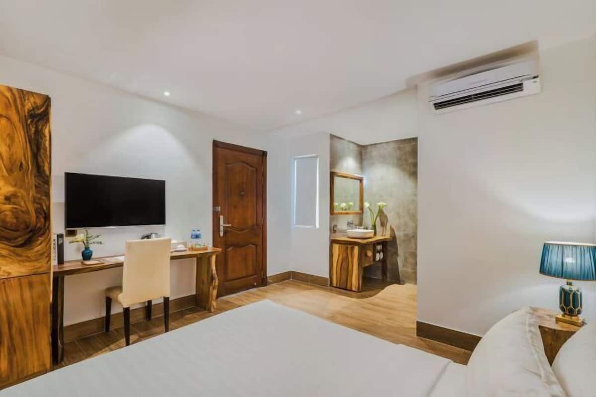 A hotel room with a bed, a desk, a TV, a mirror, and an air conditioning unit.
