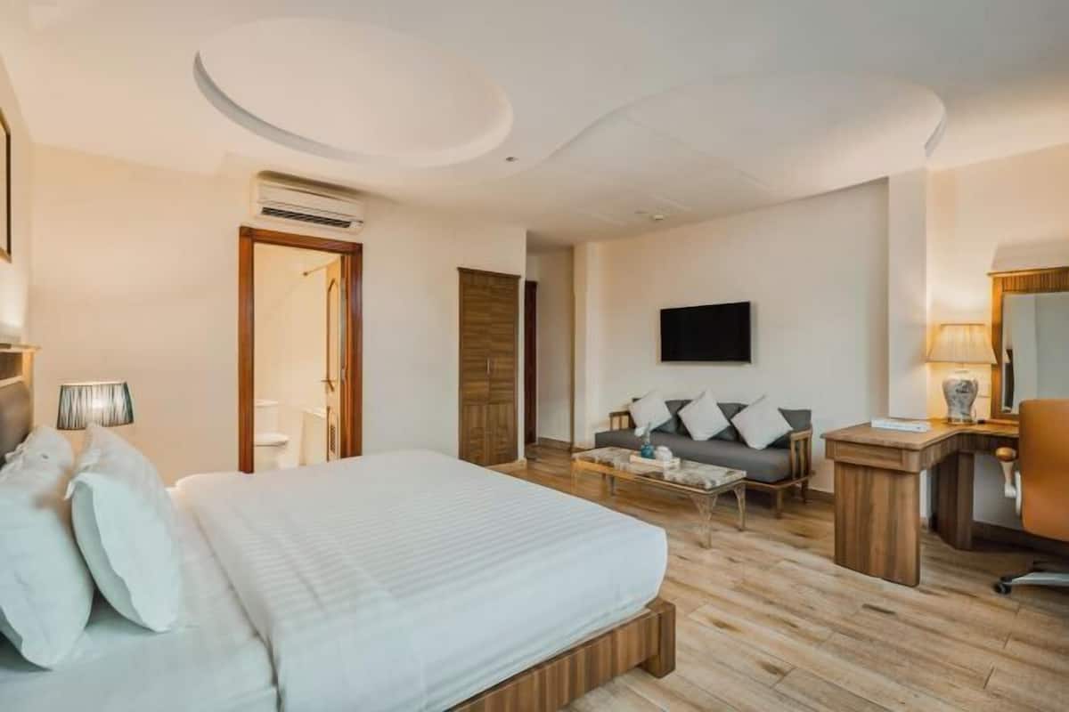 A hotel room with a bed, a sofa, a TV, a desk, and a mirror.