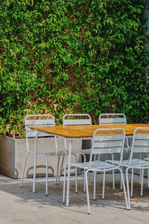 Un conjunto de mesa y sillas al aire libre, con una jardinera de concreto y un seto al fondo.