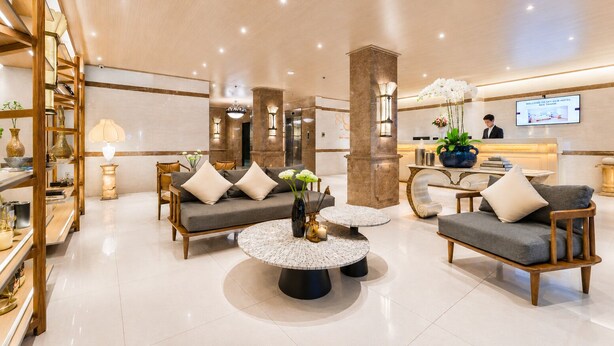 A modern hotel lobby with a reception desk, seating area with sofas and a coffee table, and a reception area with a TV screen.