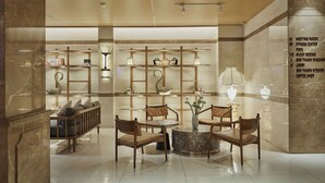 A hotel lobby with a seating area, shelves with decorative items, and a marble wall with room numbers.