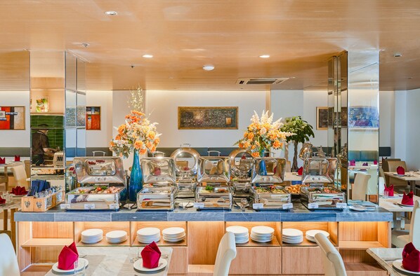 A buffet setup with multiple food stations, a mirror reflecting the room, and a dining area with chairs and tables. - Sky Gem Hotel - Ben Thanh (Ho Chi Minh City)