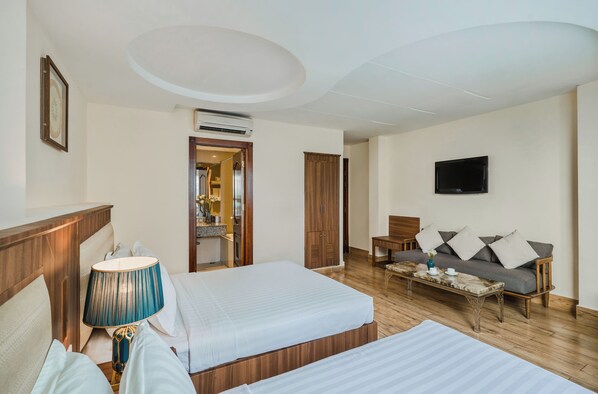 A hotel room with two beds, a television, a sofa, and a dining table.