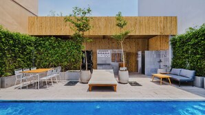 A poolside area with a wooden deck, lounge chairs, a table, and a sofa.