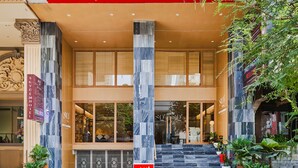 A hotel entrance with a red awning, large windows, and a staircase leading to the entrance.