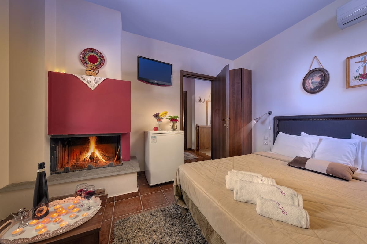 Une chambre d’hôtel avec une cheminée, un lit avec une literie blanche et marron, un petit réfrigérateur et un téléviseur fixé au mur.