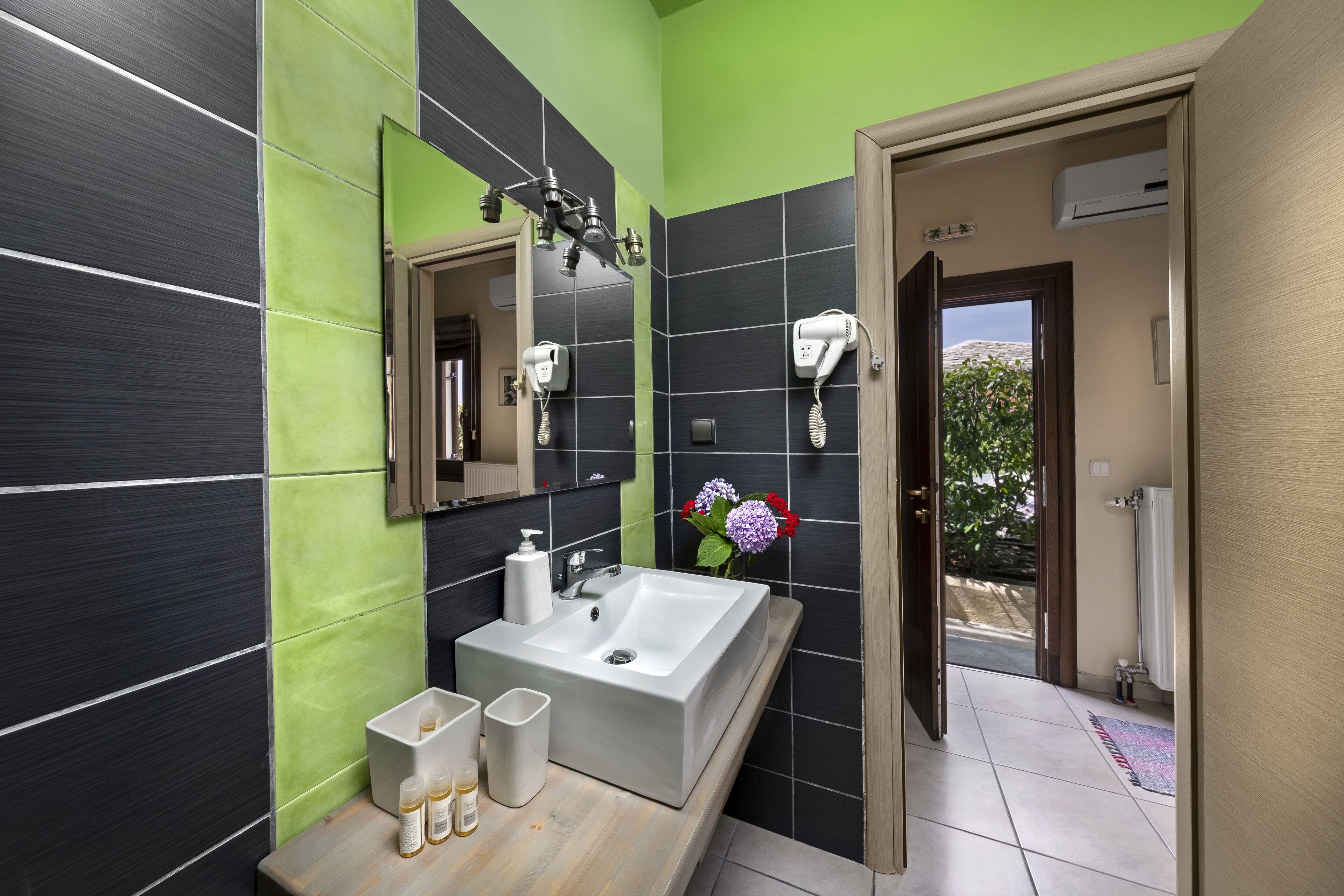 A modern bathroom with a large sink, a mirror, and two hair dryers mounted on the wall.