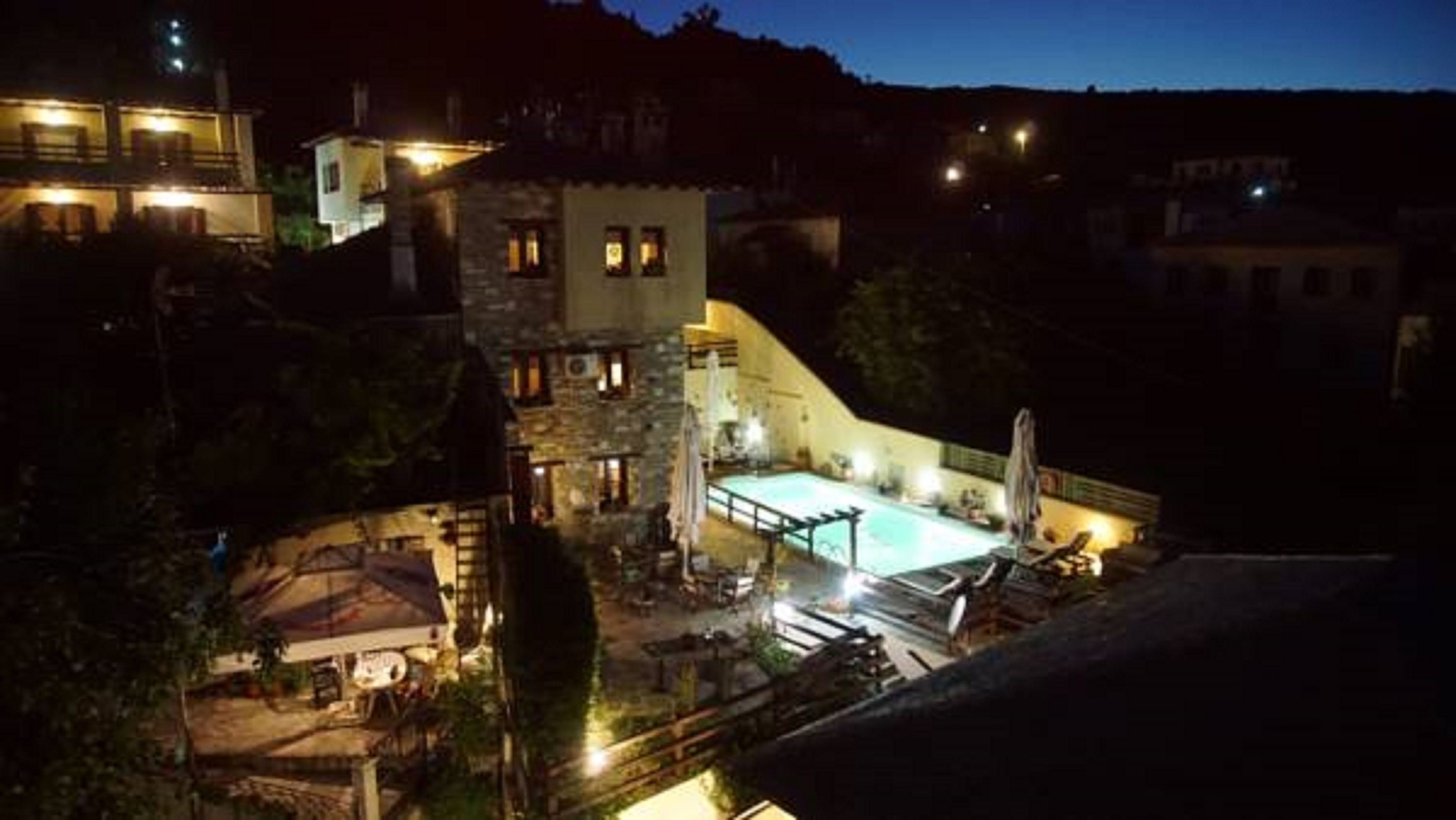 Vue nocturne d’un complexe hôtelier avec une piscine, un bâtiment en pierre et une chaîne de montagnes en arri ère-plan.