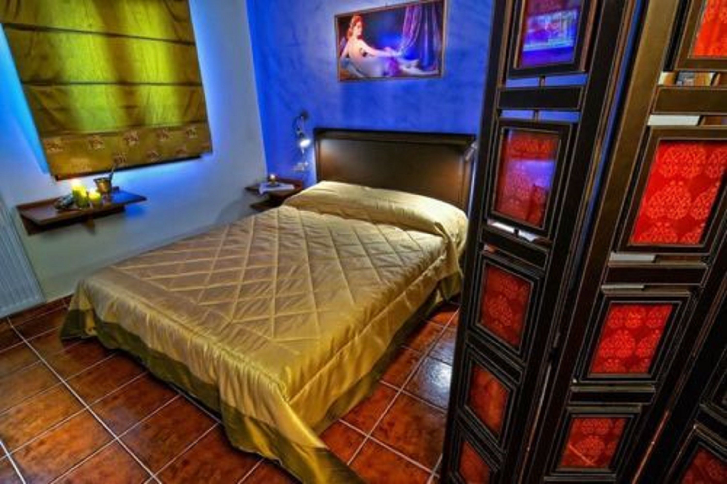 Una habitació amb un llit, una petita taula de nit, una finestra amb cortines i una paret decorada amb quadres.