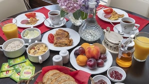 Une table de petit-déjeuner avec divers aliments, un vase de fleurs et une vue sur l’extérieur.