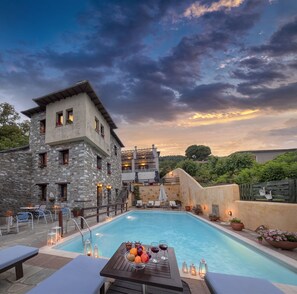 A pool area with stone buildings, outdoor seating, and a sunset view.