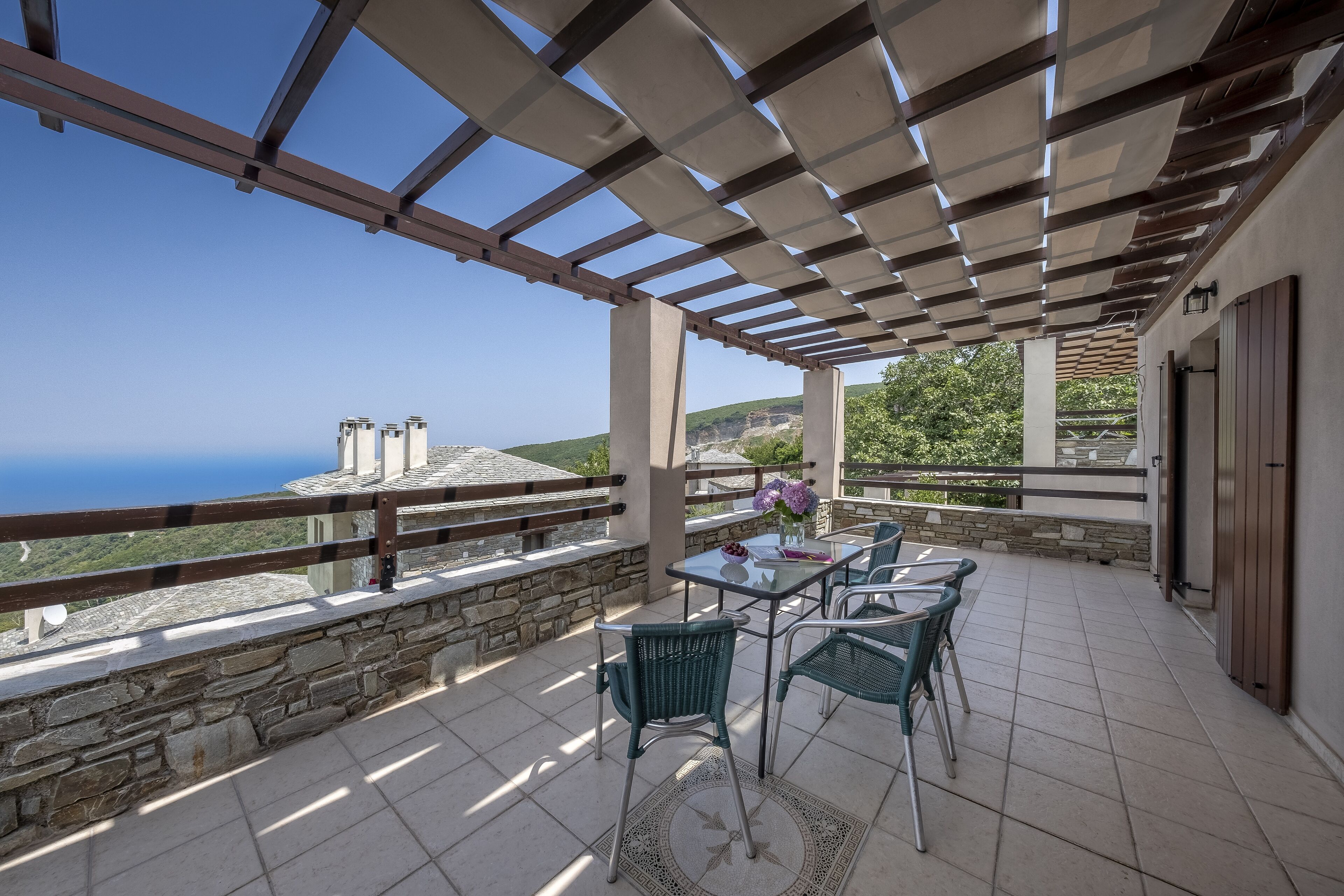 Un patio cubierto con mesa y sillas, paredes de piedra y vista al mar.