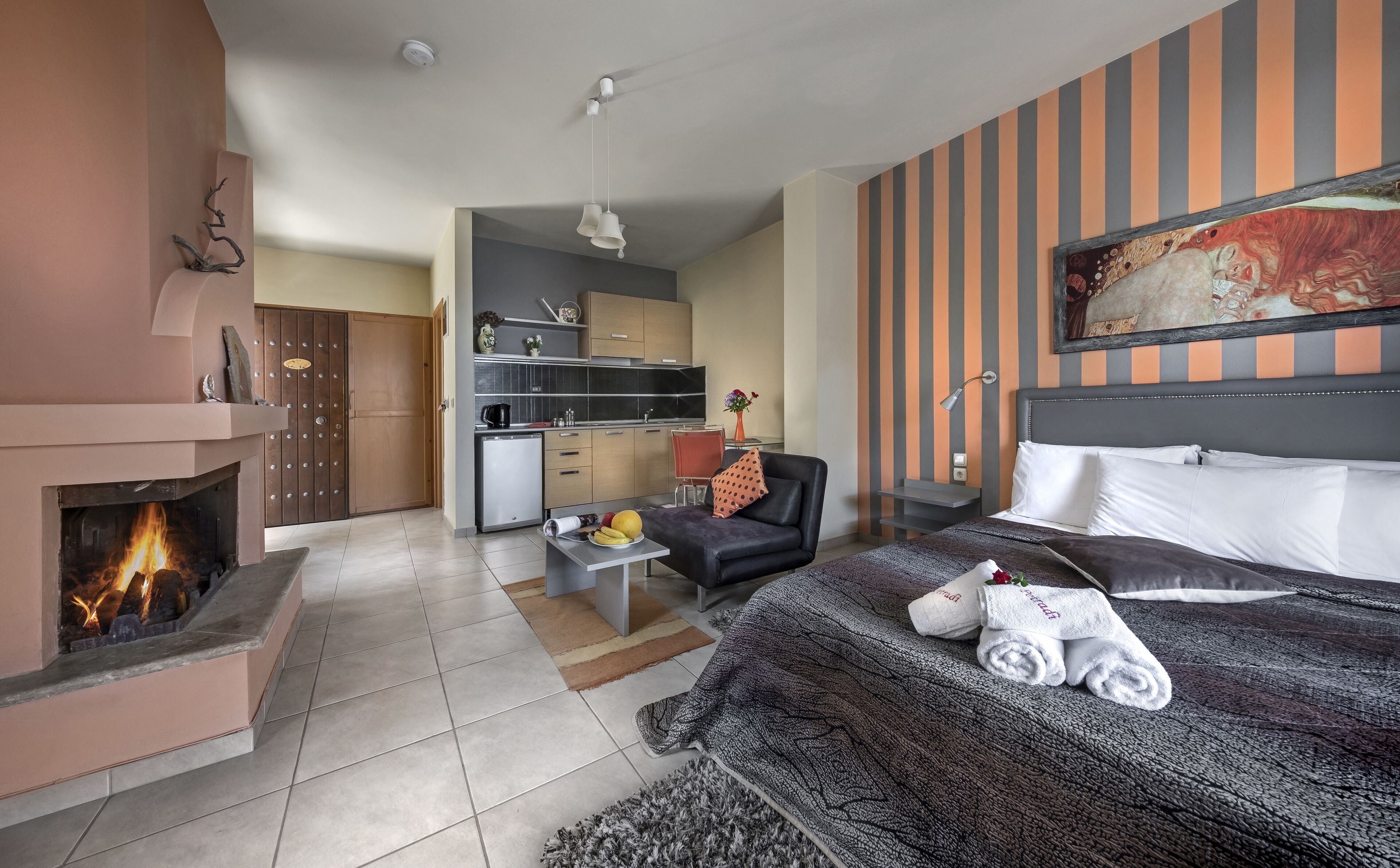 Ein Hotelzimmer mit Kamin, einem Bett mit Handtüchern, einem Schreibtisch mit Computer und einer Küchenzeile.