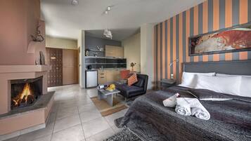 A hotel room with a fireplace, a bed with towels, a desk with a computer, and a kitchen area.