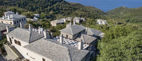A cluster of traditional stone buildings with terracotta roofs, surrounded by lush greenery and overlooking a coastal landscape.