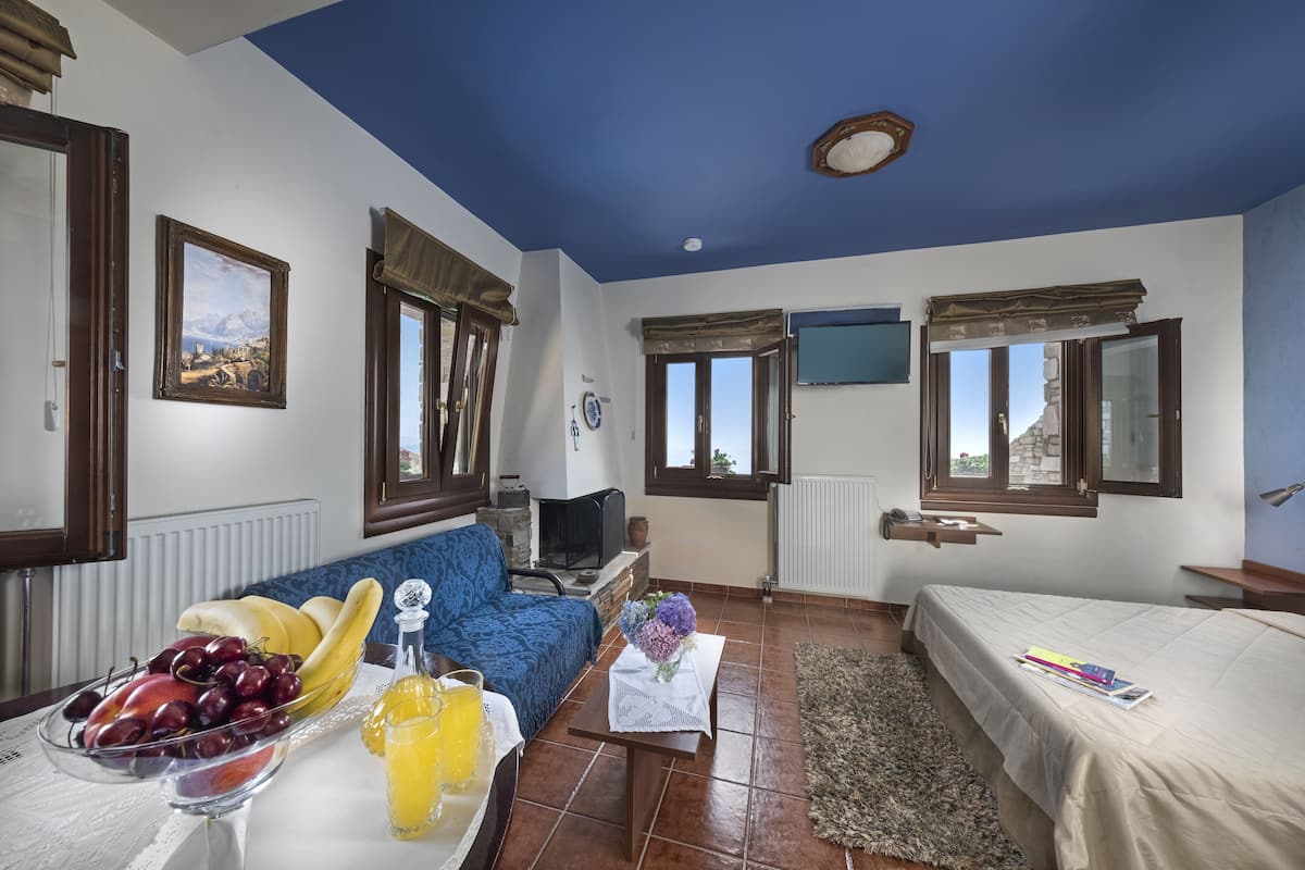 Un salon confortable avec un plafond bleu, un canapé, une table à manger avec des fruits et des boissons, un téléviseur et un lit.