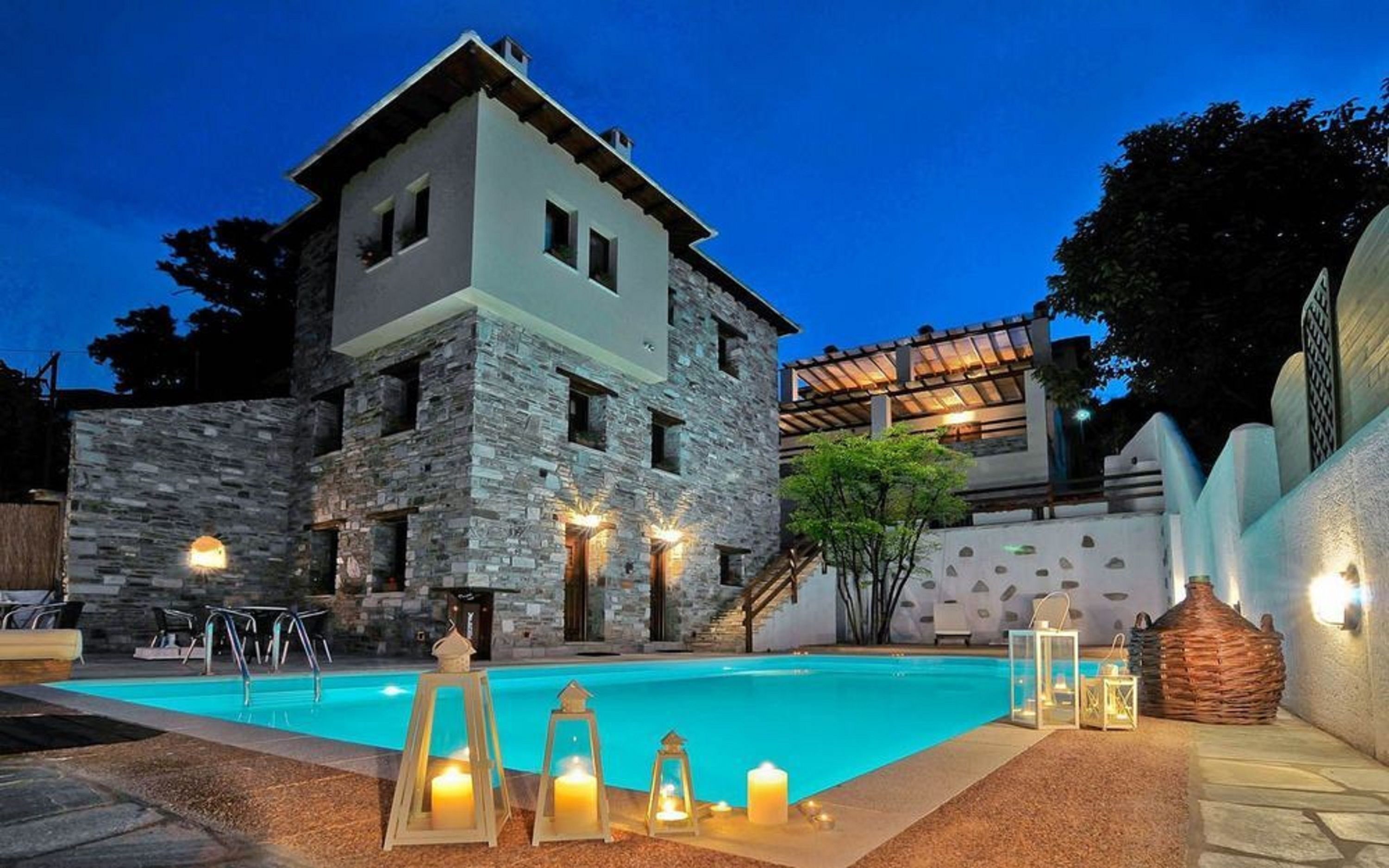 A two-story stone building with a swimming pool, outdoor lighting, and a covered patio area.