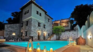 A two-story stone building with a swimming pool, outdoor lighting, and a covered patio area.