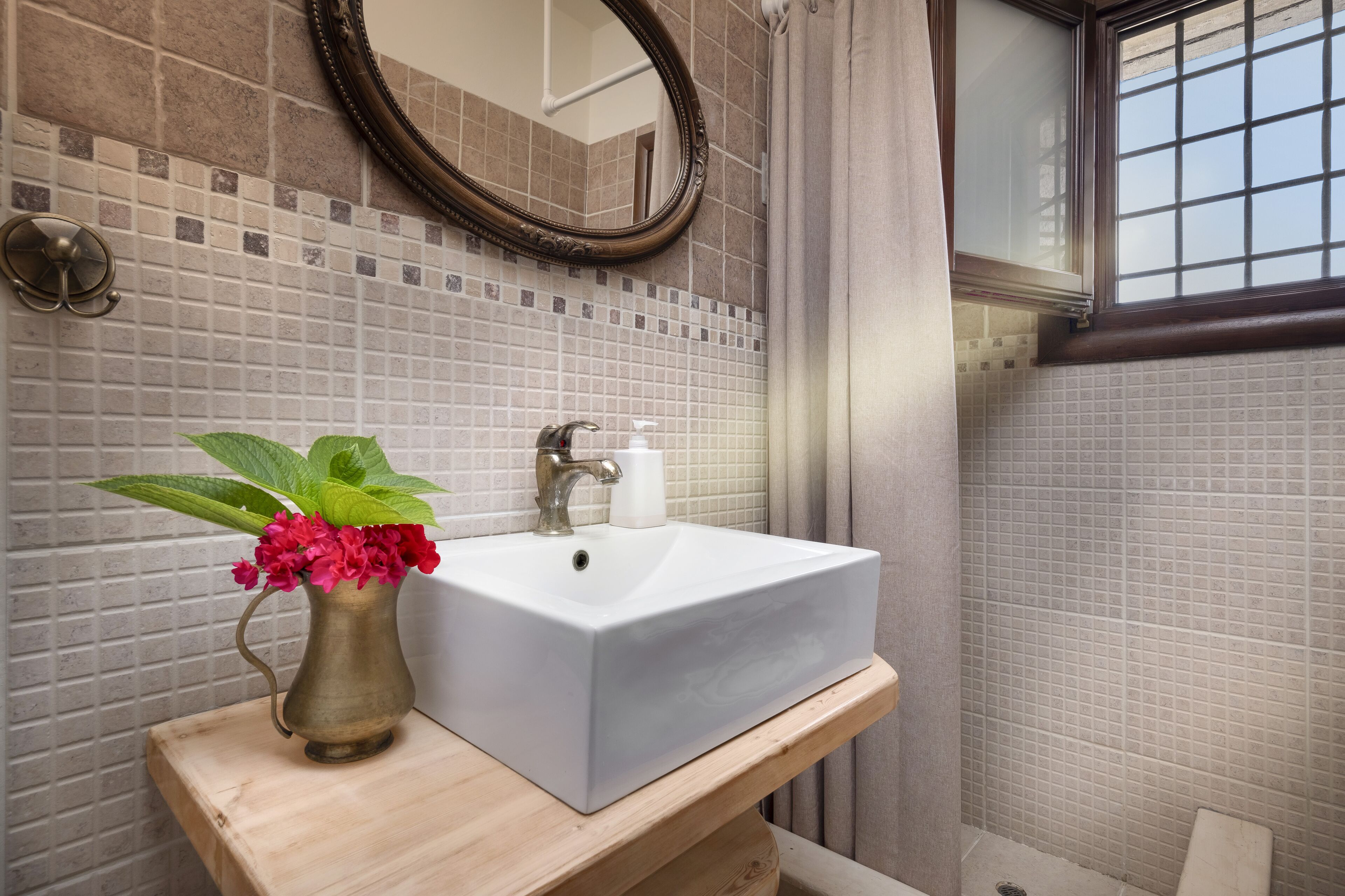 Ein Badezimmer mit einem weißen Waschbecken, einem Spiegel und einer Blumenvase.
