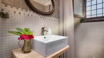 Ein Badezimmer mit einem weißen Waschbecken, einem Spiegel und einer Blumenvase.