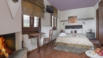 Ein Schlafzimmer mit Bett, Nachttisch, Stuhl, Kamin, Fernseher und einer kleinen Küchenzeile mit Wasserkocher.