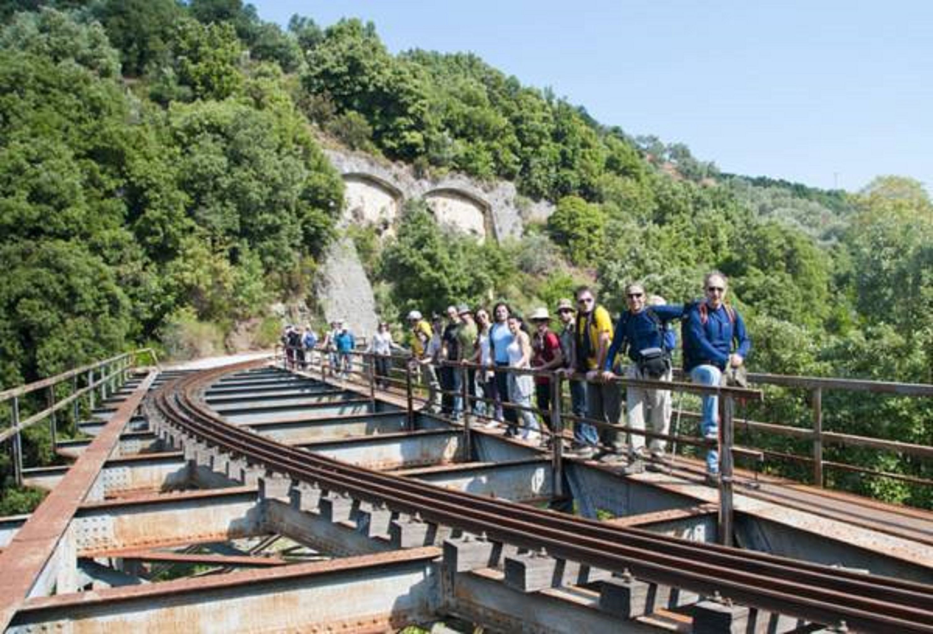 A group of people standing on a railway bridge with a mountainous backdrop.