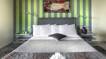 Une chambre moderne avec un grand lit, des murs à rayures vertes et grises, un tableau décoratif, deux tables de chevet avec des lampes et un arrangement floral décoratif.