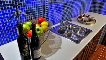 A kitchen with a blue tiled backsplash, a sink, and a fruit bowl containing apples and oranges.