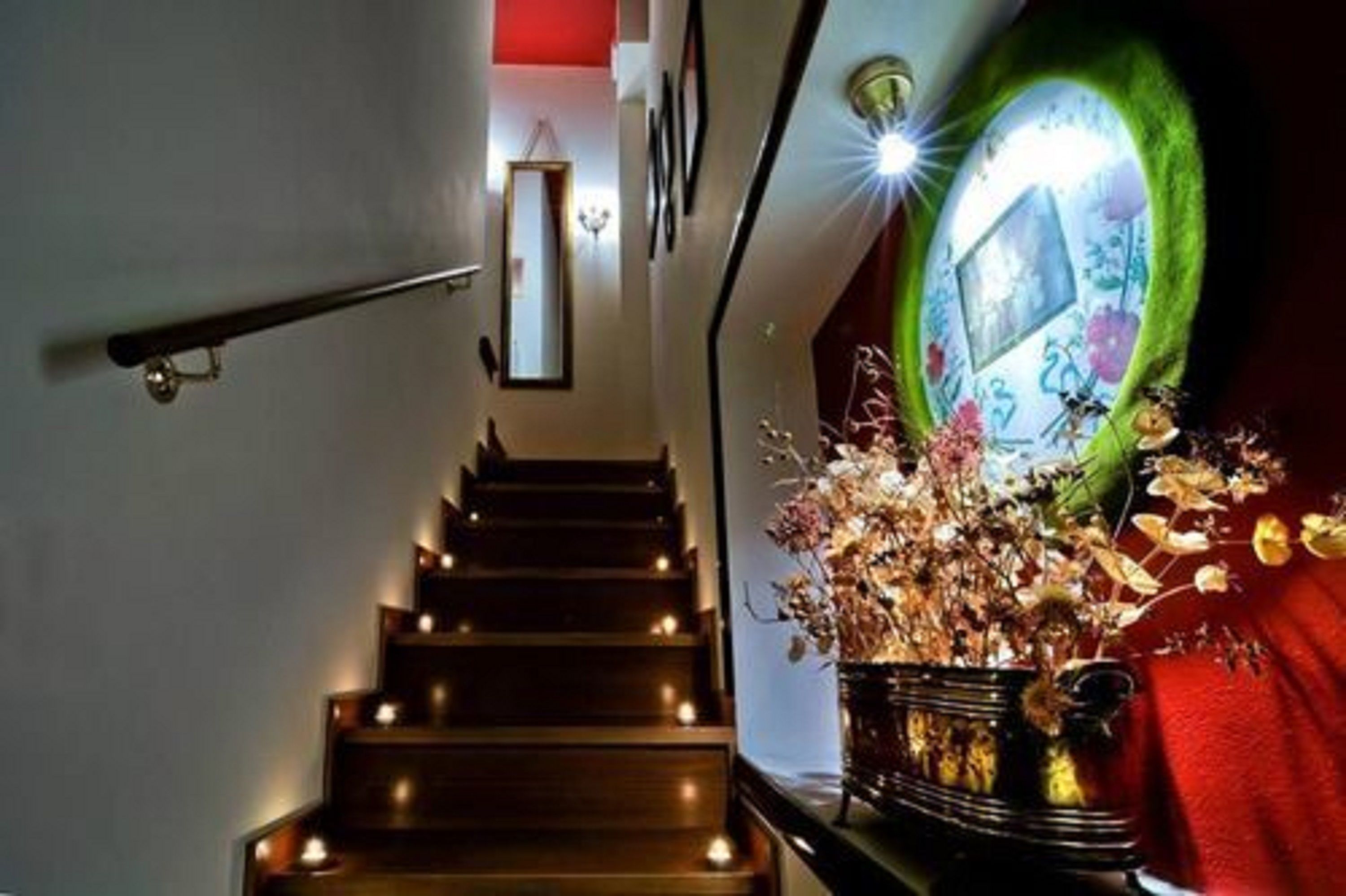 Una escalera con barandilla, un aplique de pared y un jarrón decorativo con flores secas.