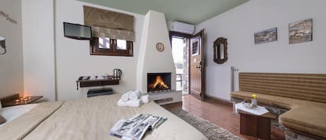 A bedroom with a large bed, a fireplace, a television, and a bench.
