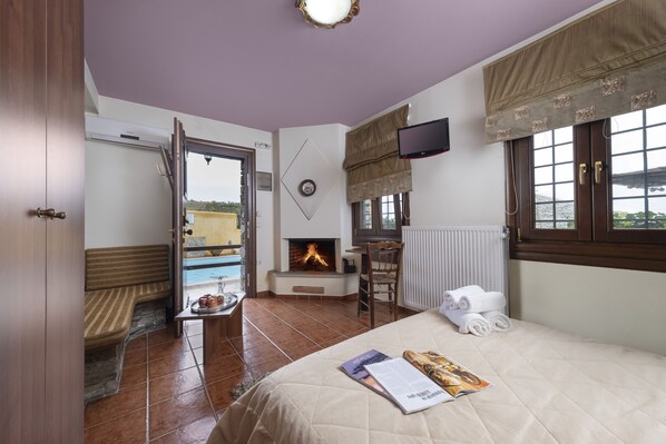 A hotel room with a bed, a small table with a tray of items, a chair, a TV mounted on the wall, and a view of the outside through a window.