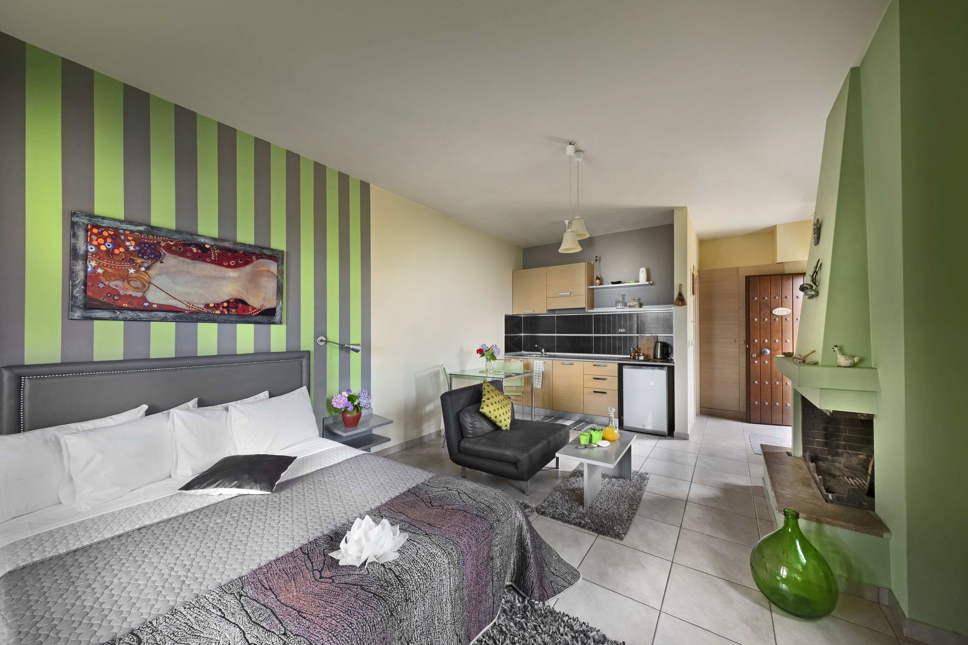 A modern hotel room with a large bed, a sofa, a dining area, and a kitchen in the background.
