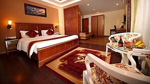 A hotel room with a large bed, a wooden headboard, a red and gold patterned rug, a dining area with a table and chairs, and a painting on the wall. - Quality Inn Woodside (Woodside)