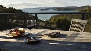 A table with a meal and a glass of red wine, overlooking a scenic view of a lake and hills. - The Sanctuary @ Bay of Islands (Opua)