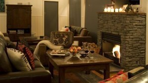 A cozy living room with a stone fireplace, leather furniture, and a coffee table with fruits and glasses. - The Sanctuary @ Bay of Islands (Opua)