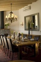 Un comedor con una larga mesa de madera, varias sillas, una araña y una chimenea de piedra.