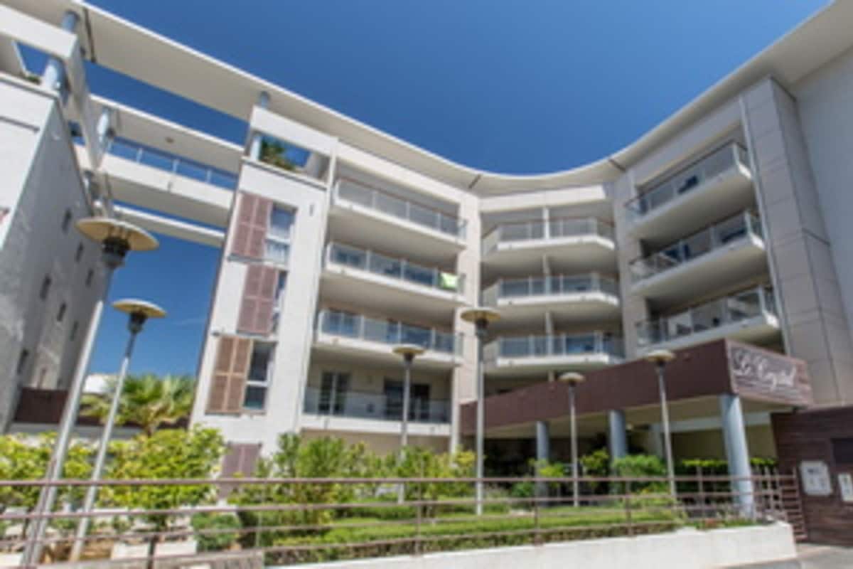 A multi-story hotel with balconies, a clear sky, and a landscaped area with a fence.