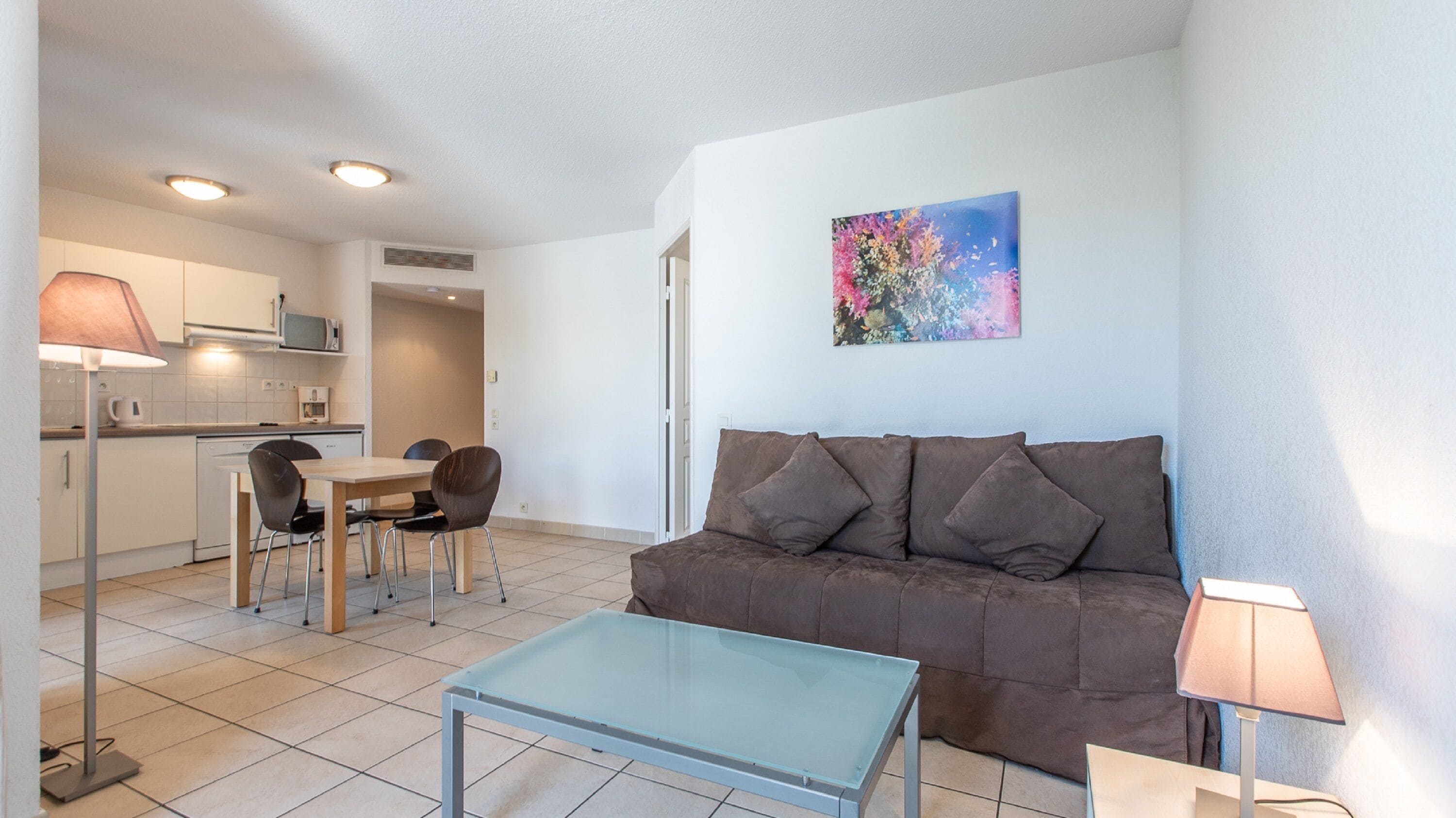 Een moderne woonkamer met een bruine bank, een glazen salontafel en een eethoek met stoelen en een tafel.